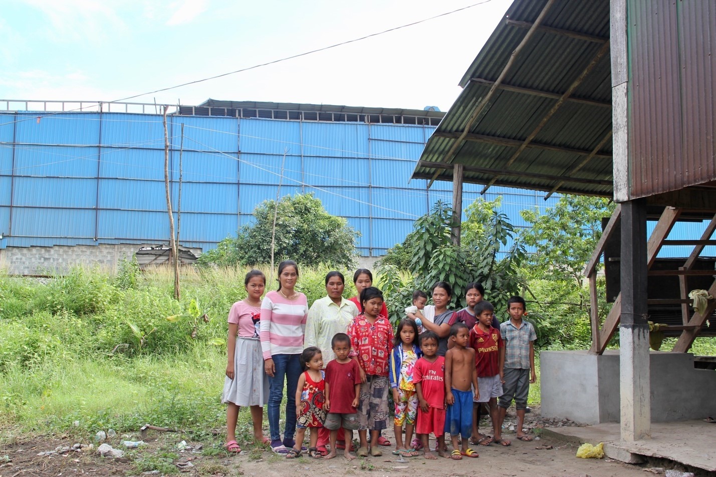 Peng Mom, Phok Nge, their children, and other neighbours with the coal ash processing plant behind them (Image: Lili Pike)